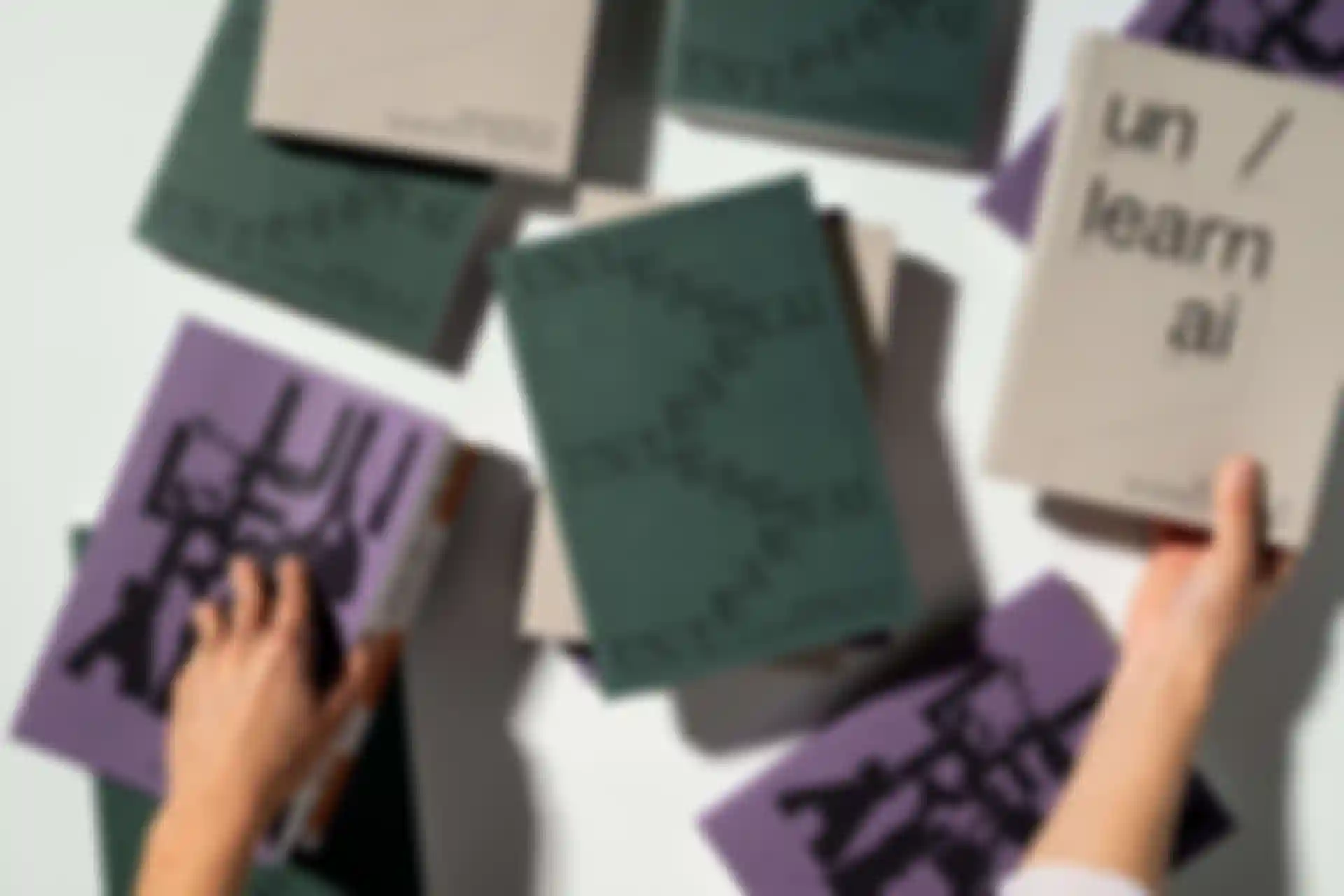 Mehrere gedruckte Exemplare aller drei Bände von un/learn ai liegen verstreut auf einem Tisch.